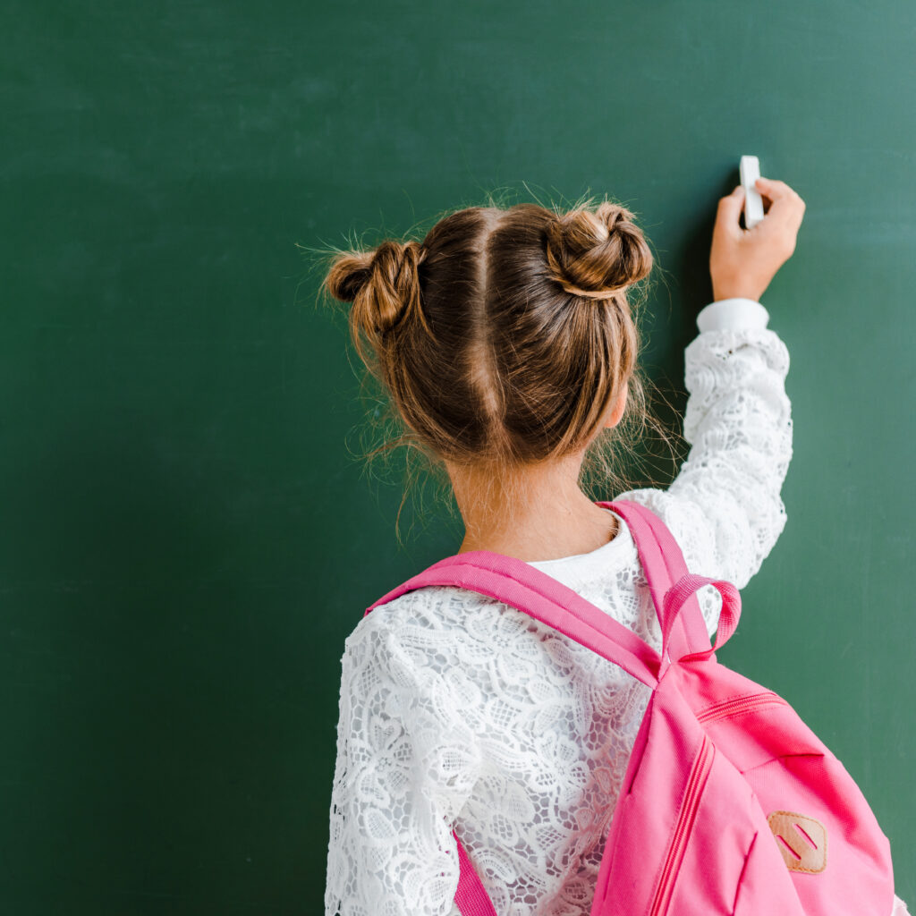 back view of kid holding chalk near chalkboard on green