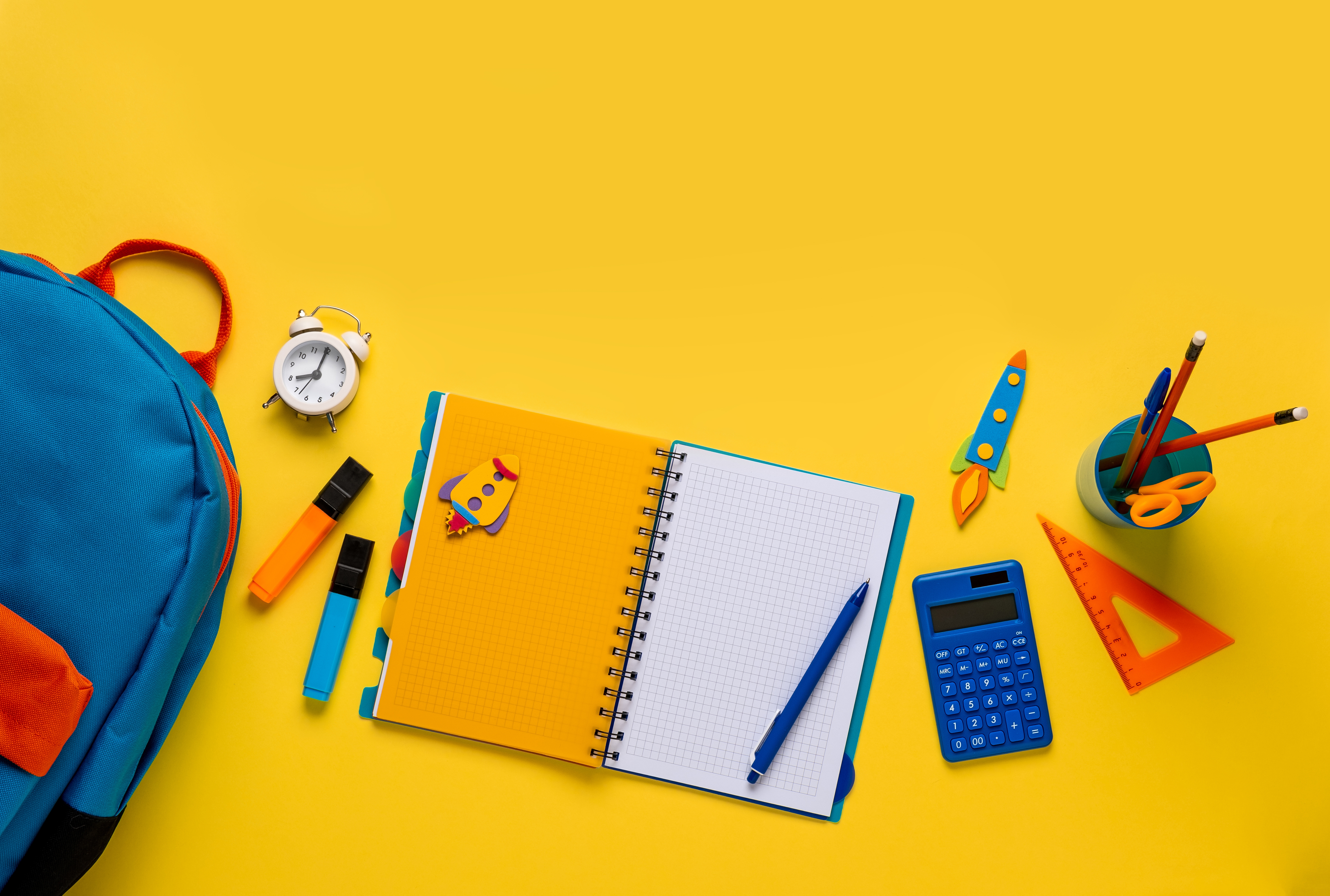 School backpack with colorful school supplies on yellow background.