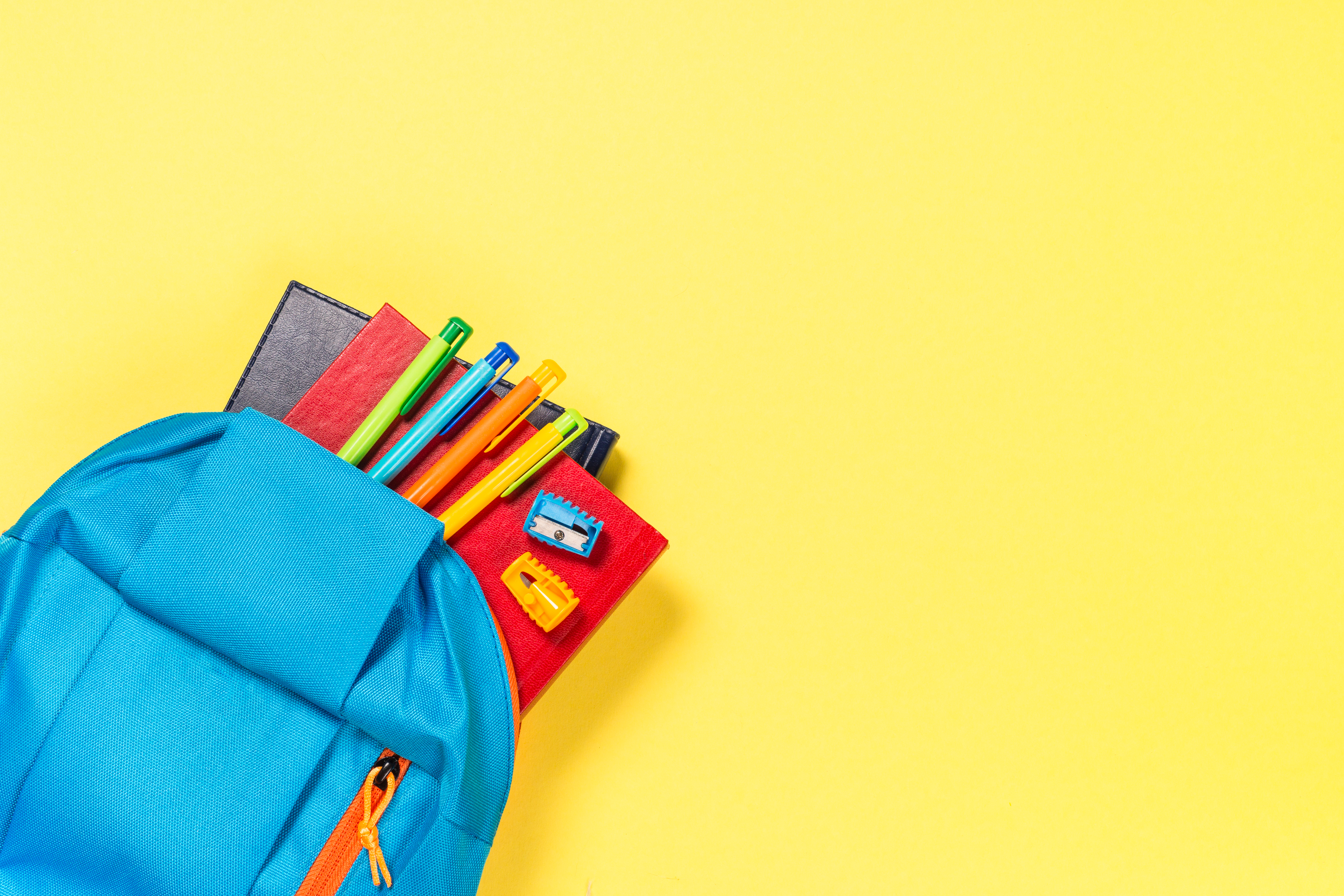 School backpack with stationery on yellow background